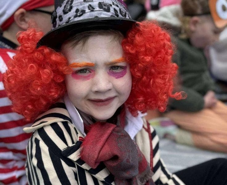 Photo of a student dressed up in a striped jacket wearing a black top hat and a red wig.