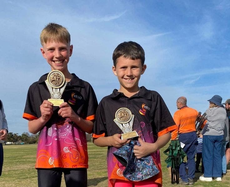 Photo of two students standing side-by-side holding athletics trophies.